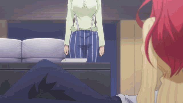 a woman with red hair is standing in front of a man laying on a couch