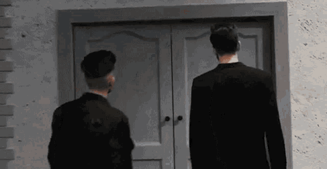 two men are standing in front of a door in a room .