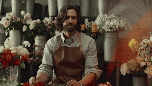 a man wearing an apron is standing in front of a bunch of flowers