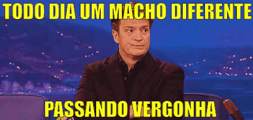 a man in a suit is sitting in front of a blue background with the words todo dia um macho diferente passando vergonha
