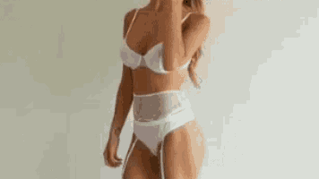 a woman in white lingerie is standing in front of a white wall with her hands on her hips .