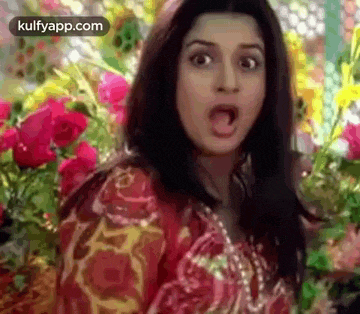 a woman is standing in front of a bunch of flowers and making a funny face .