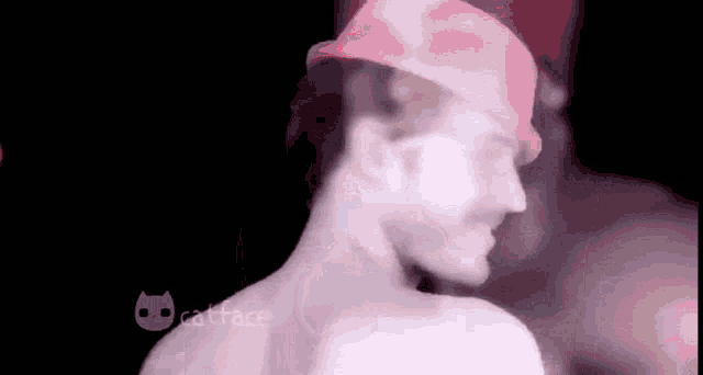 a shirtless man wearing a pink hat is standing in the dark .