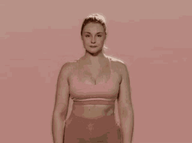 a woman in a pink sports bra and pink shorts is doing a yoga pose with her hands on her face .