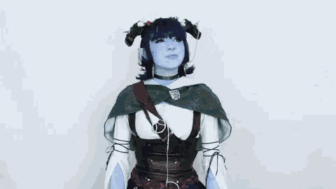 a woman in a costume with blue face paint and horns is standing in front of a white background .