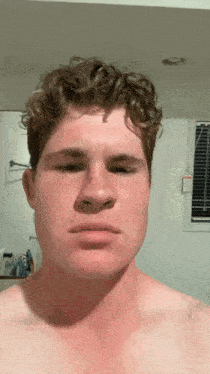 a shirtless man with curly hair looks at the camera with a serious look on his face