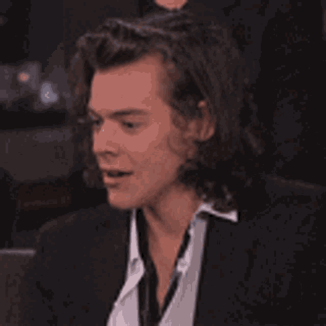 harry styles is wearing a suit and a white shirt and smiling .