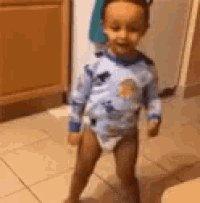 a little boy in a diaper is standing in a kitchen .