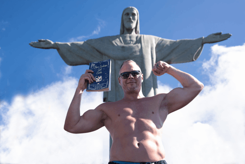 a shirtless man is holding a book in front of a statue of jesus christ