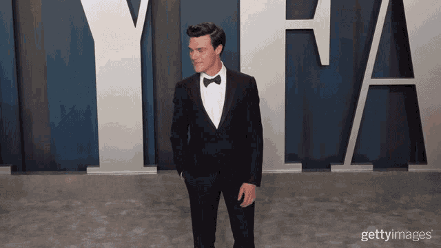 a man in a tuxedo is standing in front of a wall that says yfa
