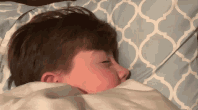 a young boy is sleeping in a bed with a blue and white pillow