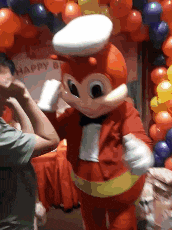 a man is standing next to a jollibee mascot in front of balloons .