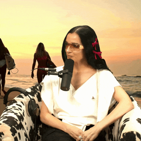 a woman wearing sunglasses sits in front of a microphone on a cow print chair