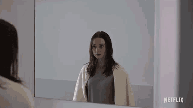a woman is standing in front of a mirror and looking at herself .