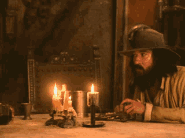 a man in a cowboy hat sits at a table with candles