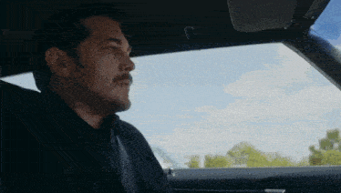 a man with a mustache is sitting in the back seat of a car looking out the window .