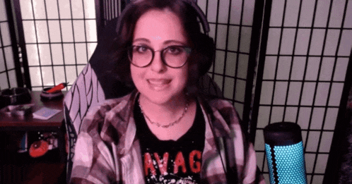 a woman wearing glasses and headphones is sitting in front of a microphone in a recording studio .