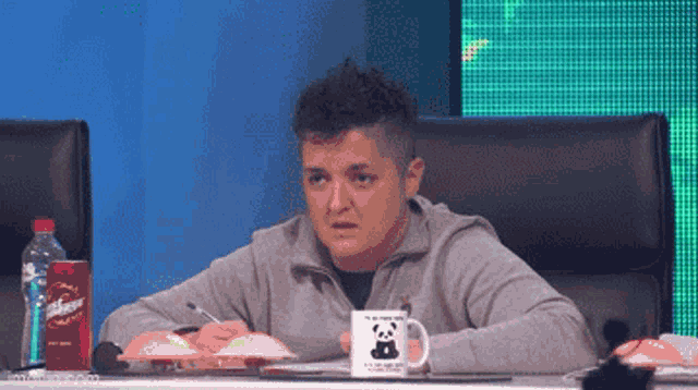 a woman sits at a table with a panda mug and a bottle of diet coke