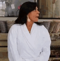 a woman wearing a white robe and earrings is sitting in front of a couch .