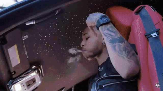 a man with a tattoo on his arm is smoking a cigarette while sitting in a car ..