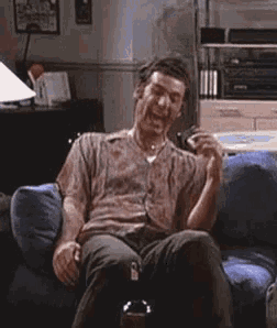 a man is sitting on a couch laughing and holding a glass of wine .
