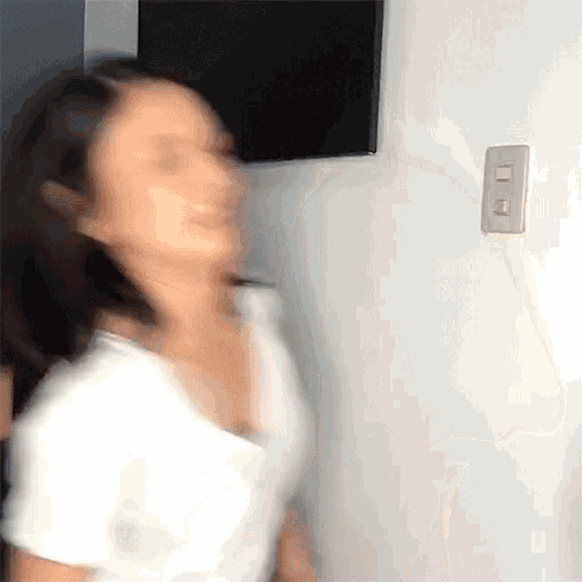 a blurry picture of a woman standing in front of a wall with a light switch on it .