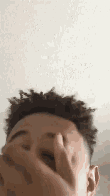 a young man is covering his face with his hand while making a funny face .