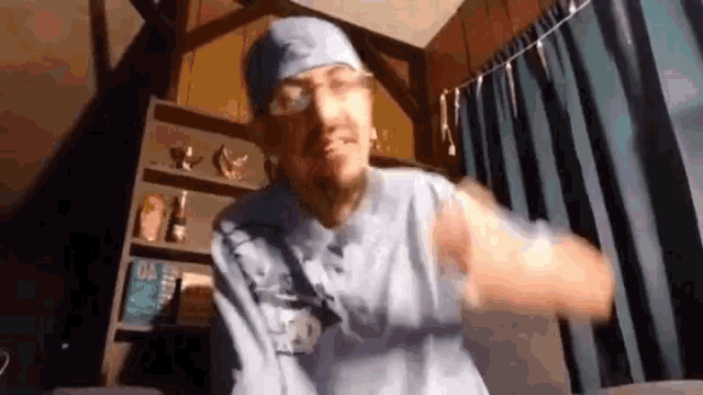 a man wearing a blue shirt and a surgical cap is dancing in a room .