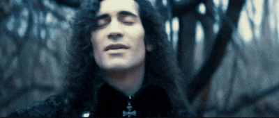 a man with long curly hair is wearing a black shirt with a cross necklace
