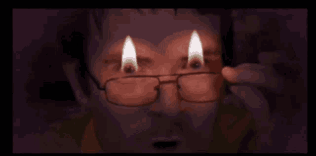 a man wearing glasses is holding a lighter in front of his eyes .
