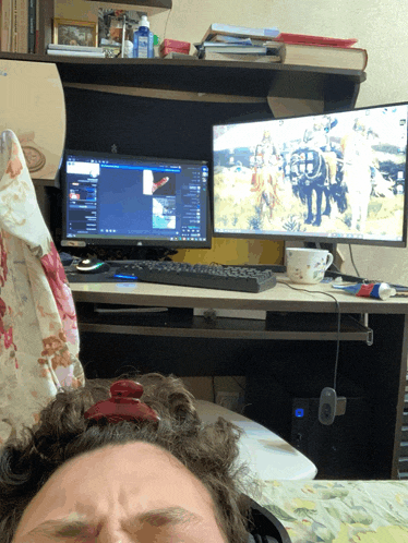 a man laying on a bed with his eyes closed in front of a desk with two monitors
