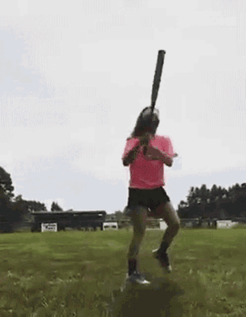 a woman in a pink shirt is holding a baseball bat and running on a field .