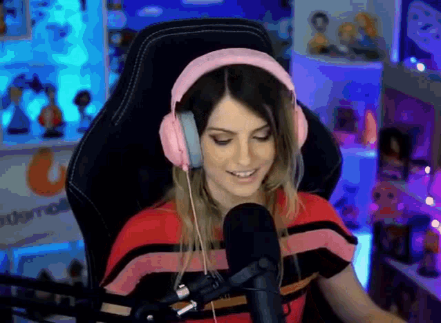 a woman wearing pink headphones is sitting in front of a microphone in a room .