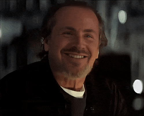 a man with a beard is smiling and wearing a white shirt