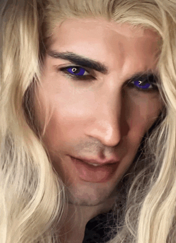 a man with long blonde hair and blue eyes looks at the camera