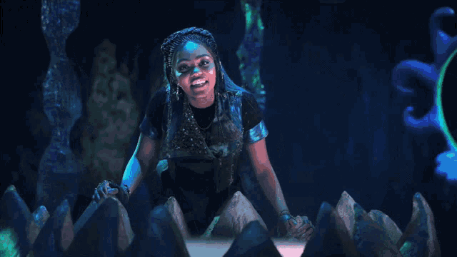 a woman with blue paint on her face stands in a dark cave