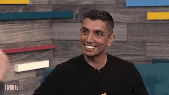 a man in a black shirt is smiling in front of a wooden wall with imdb written on it