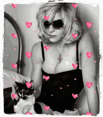 a woman wearing sunglasses and a cross necklace holds a cat