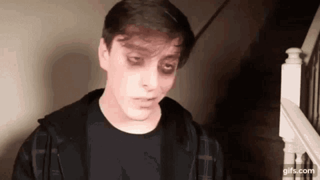 a young man with black eyes and a black shirt is standing in front of a staircase .