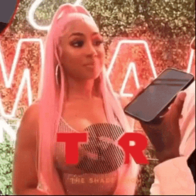 a woman with pink hair is being interviewed by a man in a suit while holding a cell phone .