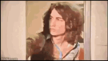 a man with long hair is standing in front of a door and looking out .