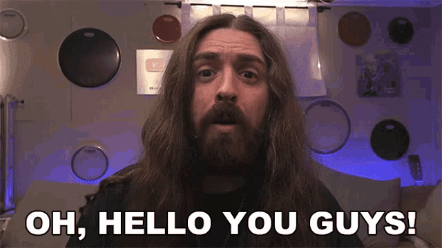 a man with long hair and a beard is saying " oh hello you guys "