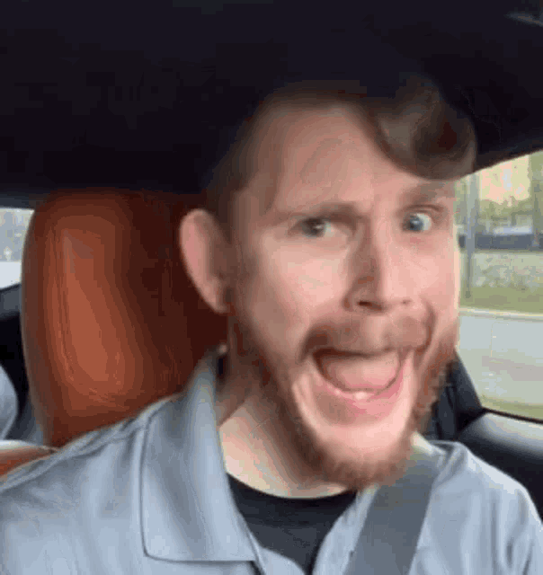 a man with a beard is making a funny face in a car .