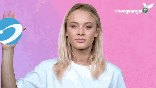 a woman in a white shirt is holding a blue circle in her hand in front of a pink background that says changeangel
