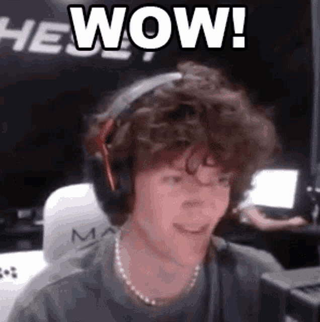 a man with curly hair is wearing headphones and smiling while sitting in front of a computer .
