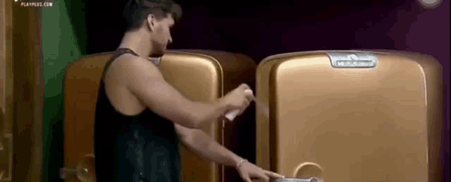 a man in a black tank top is opening a gold refrigerator door