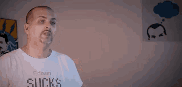 a man wearing a white shirt that says edison sucks is standing in front of a wall .