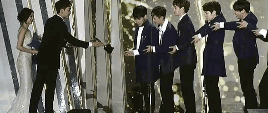 a woman in a white dress is standing next to a group of men in suits on a stage .