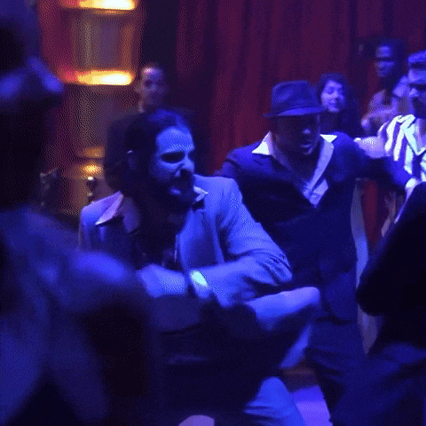 a couple of men are dancing in a dark room with a red exit sign in the background .