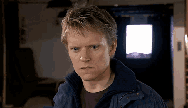 a man in a blue jacket looks at the camera with a serious look on his face